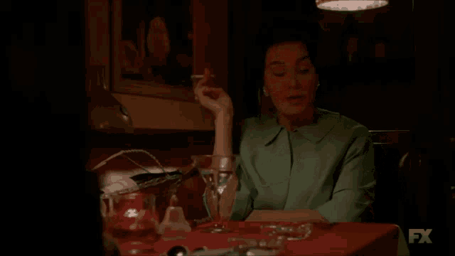 a woman is sitting at a table with a martini and a cigarette and the fx logo is visible