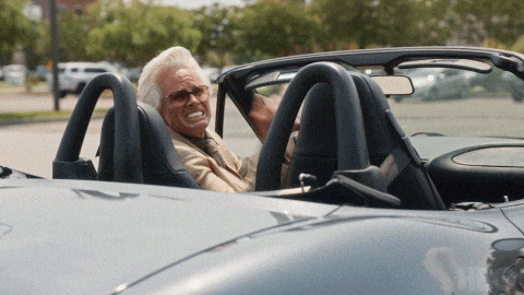 a man with glasses is sitting in a convertible sports car