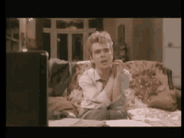 a man is sitting on a couch in front of a computer screen .