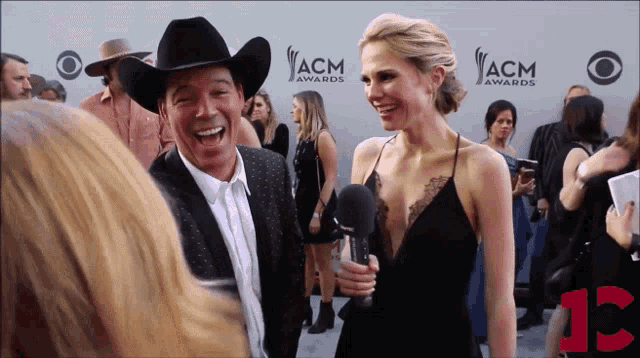 a man in a cowboy hat and a woman in a black dress are laughing on the red carpet of the acm awards