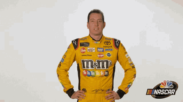 a man in a yellow m & m 's shirt stands in front of a nascar logo
