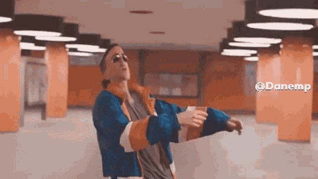 a man wearing sunglasses and a blue jacket is dancing in a subway station