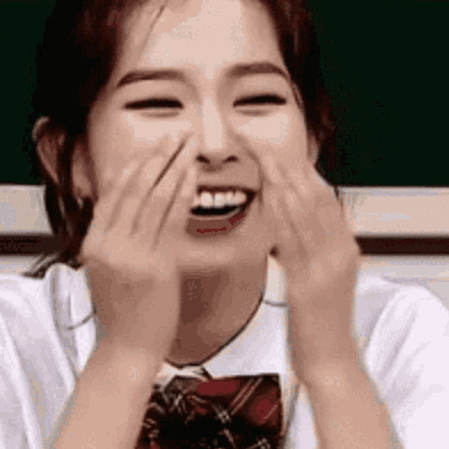 a girl is laughing with her hands on her face .