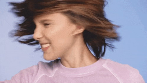 a woman wearing hoop earrings and a purple shirt is smiling while her hair blows in the wind