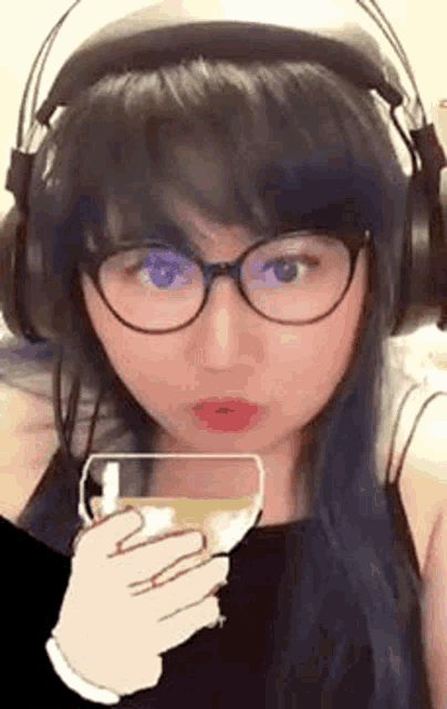 a woman wearing headphones and glasses is holding a glass of liquid .