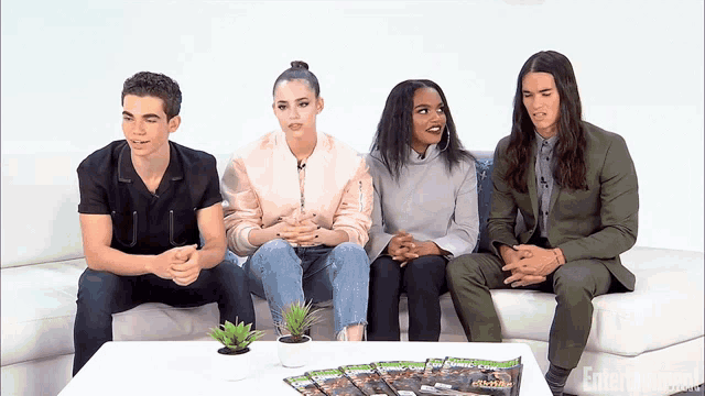 a group of people sit on a couch in front of a table with entertainment magazines