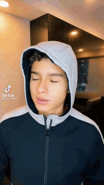 a young man wearing a hooded jacket is making a funny face .