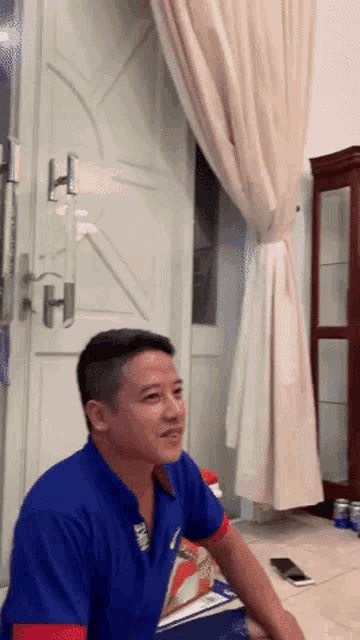 a man in a blue shirt is sitting on the floor in front of a white door