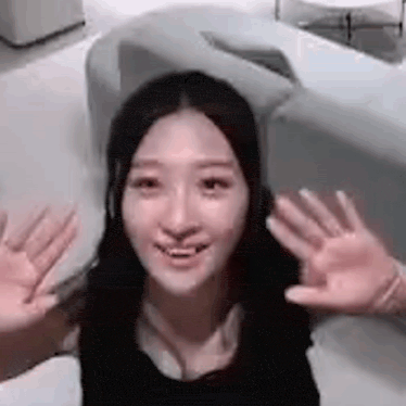 a woman is sitting on a couch with her hands up and smiling .