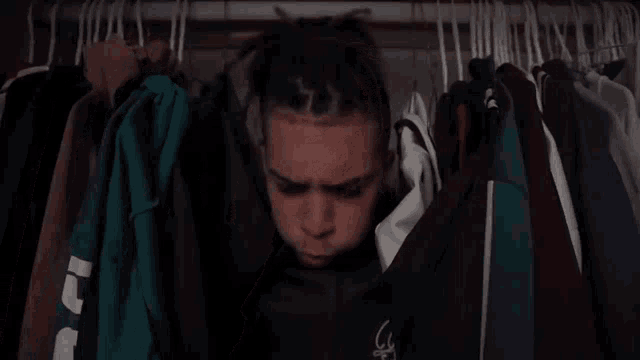 a man covering his face in front of a closet full of clothes