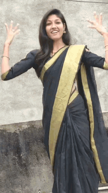 a woman wearing a black and gold striped saree stands in front of a wall