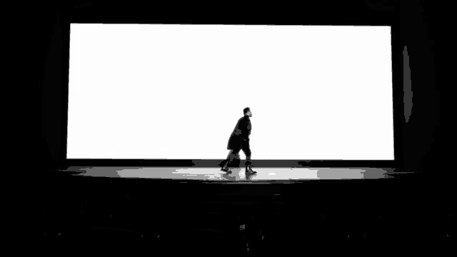 a man in a suit is walking on a stage in front of a large screen .