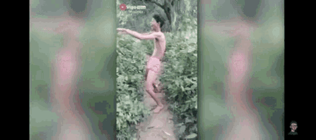 a shirtless man in pink shorts is standing on a dirt path in the woods .