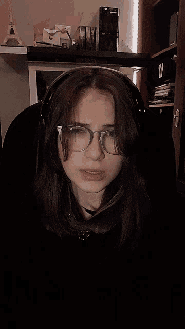 a girl wearing glasses and headphones looks at the camera in a dark room