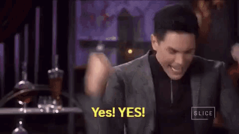 a man in a suit and black shirt is holding his fist in the air and saying yes .