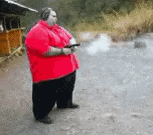 a very fat man in a red shirt is holding a gun