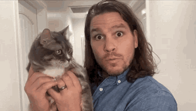 a man with long hair is holding a cat and making a funny face .