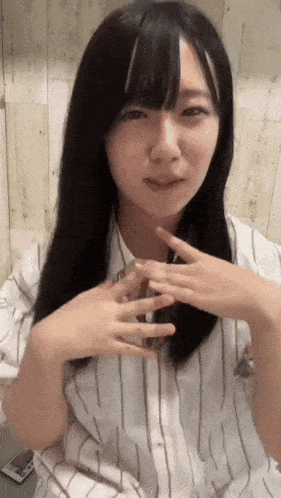 a woman with long black hair is wearing a striped shirt and has her hands on her chest