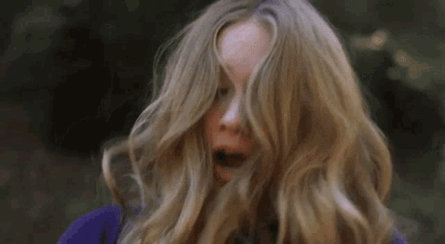 a woman with long blonde hair is holding a knife in her hand and making a funny face .