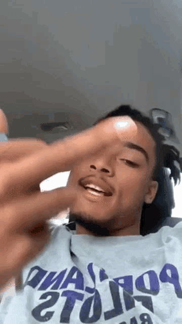 a young man with dreadlocks is sitting in a car making a funny face with his finger .