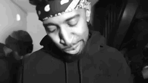 a black and white photo of a man wearing a bandana and a black hoodie .
