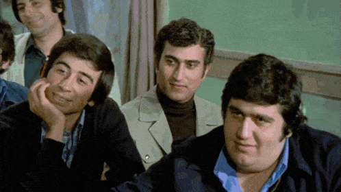 a group of men are sitting in a classroom and one of them is smiling