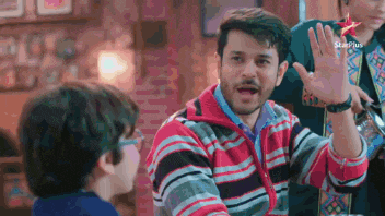 a man in a striped sweater is sitting at a table talking to another man .