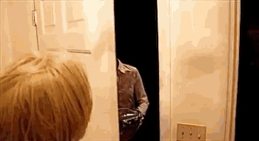a man is peeking out from behind a door while holding a gun .