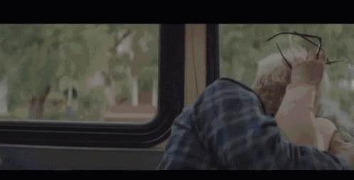 a man is adjusting his glasses while sitting on a bus looking out the window .