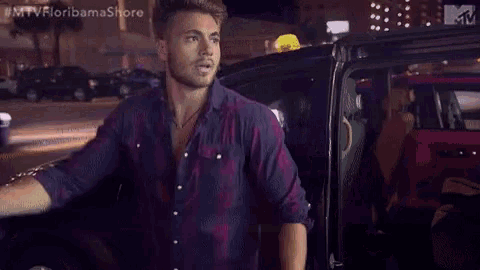a man in a purple plaid shirt is standing in front of a pink car .