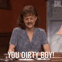 a woman with a mustache is sitting at a desk and saying you dirty boy
