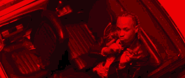 a man in a leather jacket is sitting in the back seat of a red car .