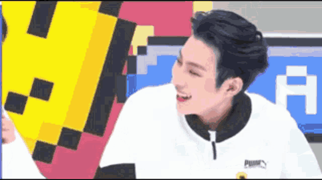 a man in a white puma shirt is smiling in front of a pixelated background