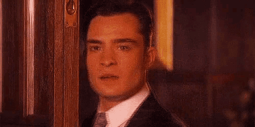 a man in a tuxedo is peeking out of a doorway .