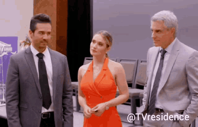a woman in an orange dress is standing between two men in suits and ties