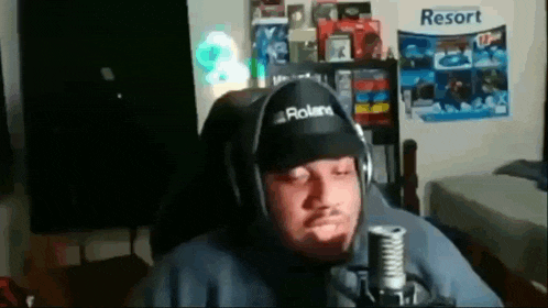 a man wearing a roland hat and headphones is sitting in front of a microphone in a room .