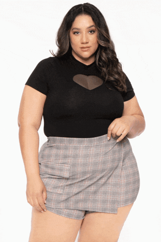 a plus size model wearing a black top and plaid skirt