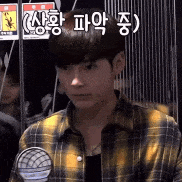 a young man wearing a plaid shirt stands in front of a sign with chinese writing on it