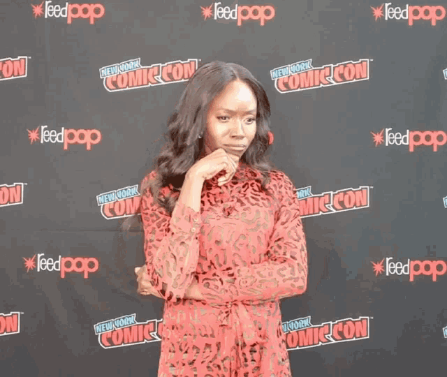 a woman in a red dress stands in front of a wall that says comic con