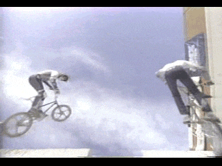 a man on a bike is doing a trick while another man on a skateboard looks on