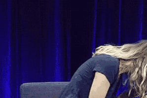 a woman is sitting on a chair in front of a blue curtain with her head down .