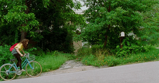a girl is riding a bike down a grassy hill