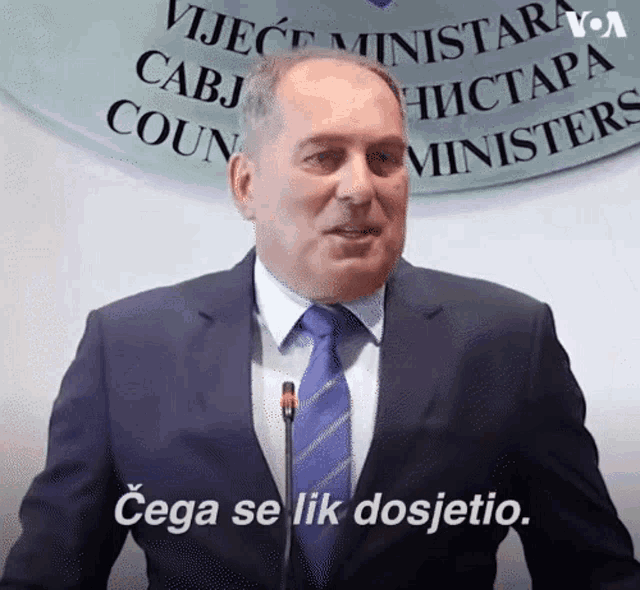 a man in a suit and tie stands in front of a sign that says vijjece ministriara