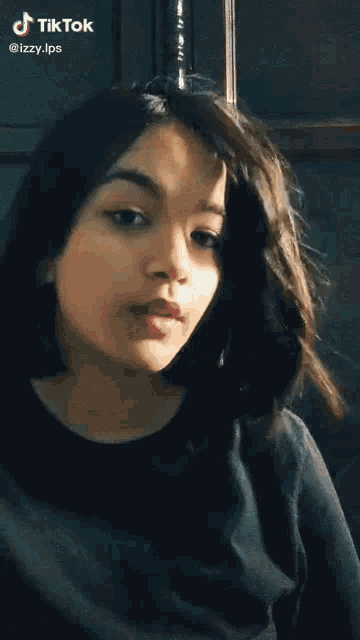 a girl with long dark hair is wearing a black shirt and making a funny face .