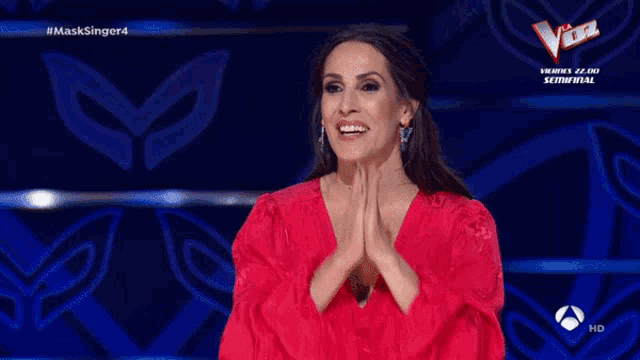 a woman in a red dress is smiling in front of a blue background that says the voice