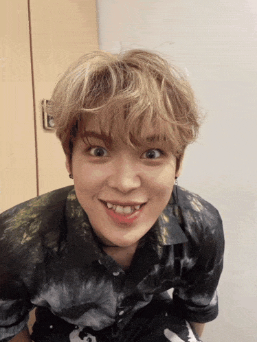 a young man wearing a tie dye shirt is making a funny face with his mouth open