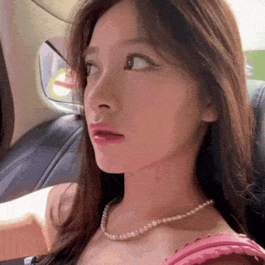 a woman wearing a pink top and a pearl necklace is sitting in the back seat of a car .