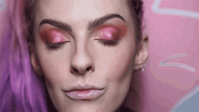 a close up of a woman 's face with pink eye shadow and pink hair .