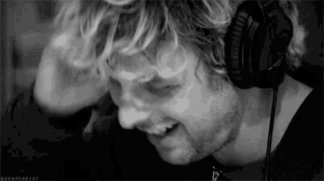 a man with curly hair is wearing headphones and smiling .