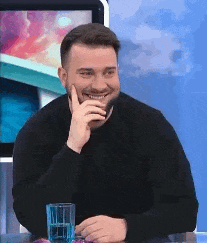 a man with a beard is sitting at a table with a glass of water and laughing .
